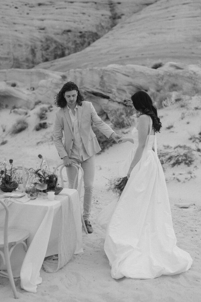 Groom helping the bride into her chair at their wedding reception at Amangiri in the southern Utah desert. 