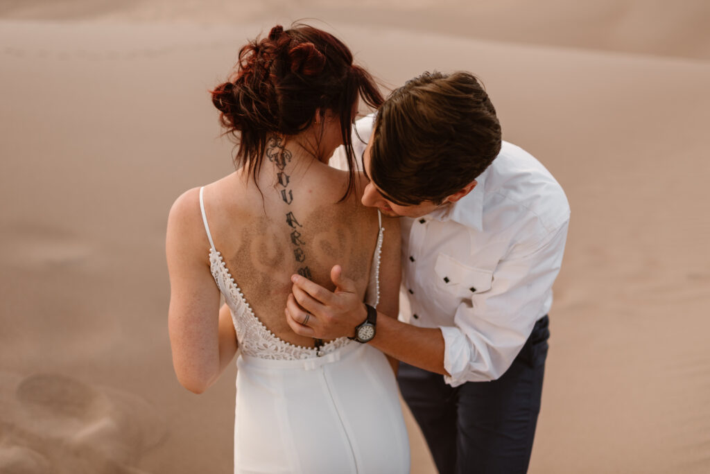 An elopement in Colorado's Great Sand Dunes National Park. A sweet moment between the couple as he draws hearts in the sand pressed onto her back.