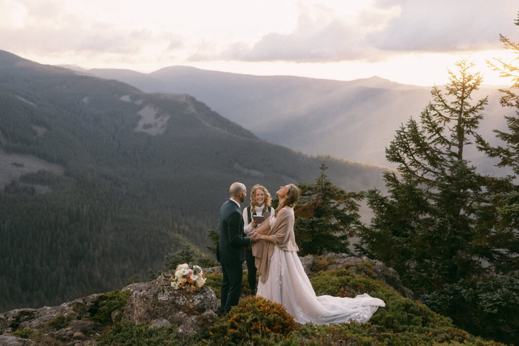 A couple experiencing on of the benefits of eloping while exchanging vows on top of a mountain in the Columbia River Gorge with their best friend officiating.