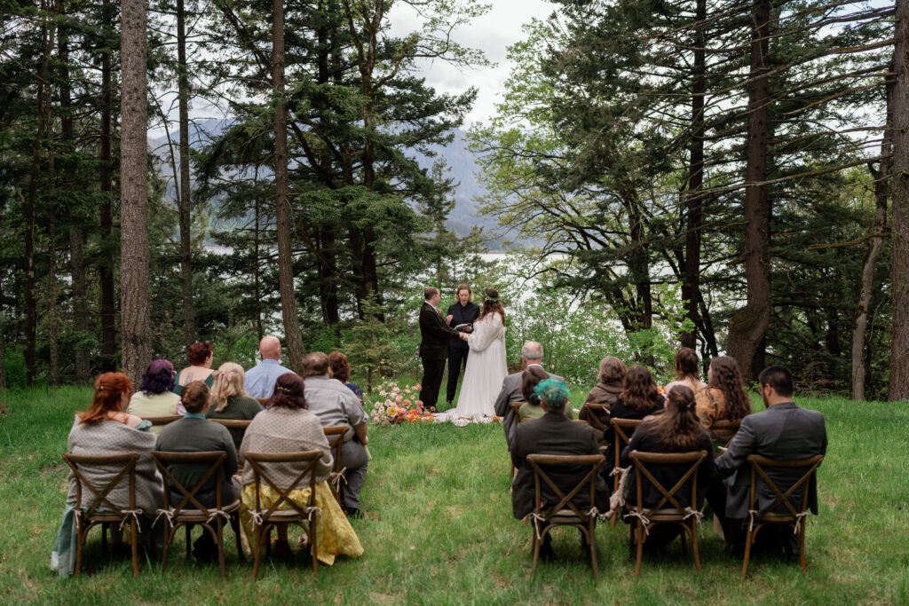 small wedding ceremony in a forest in oregon, family seated in chairs and watching as a bride and groom exchange wedding vows