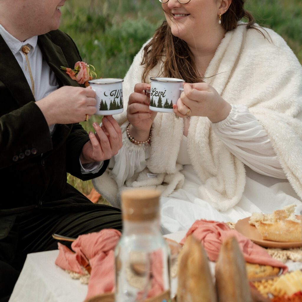 couple cheersing mugs with their names on their wedding at a luxury elopement picnic