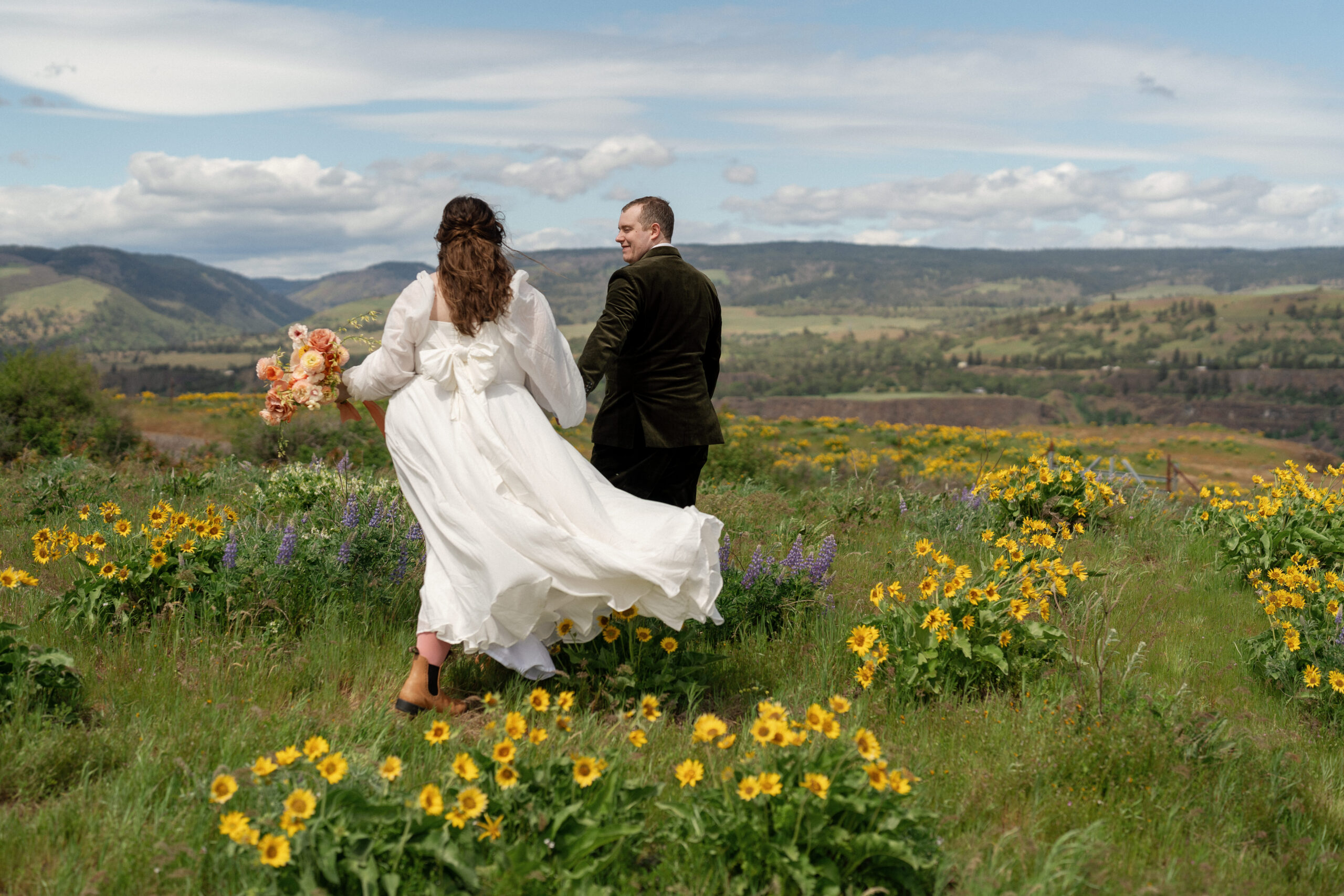 bride and groom walking through a breezy wildflower filled meadow in oregon on their small wedding day