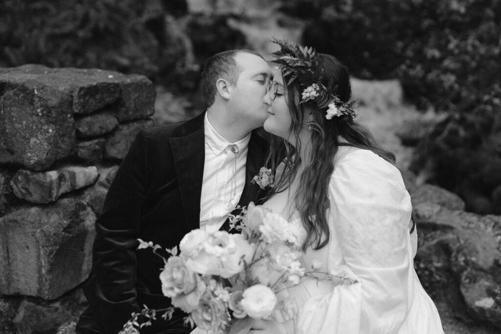 black and white portrait of groom kissing bride on her cheek